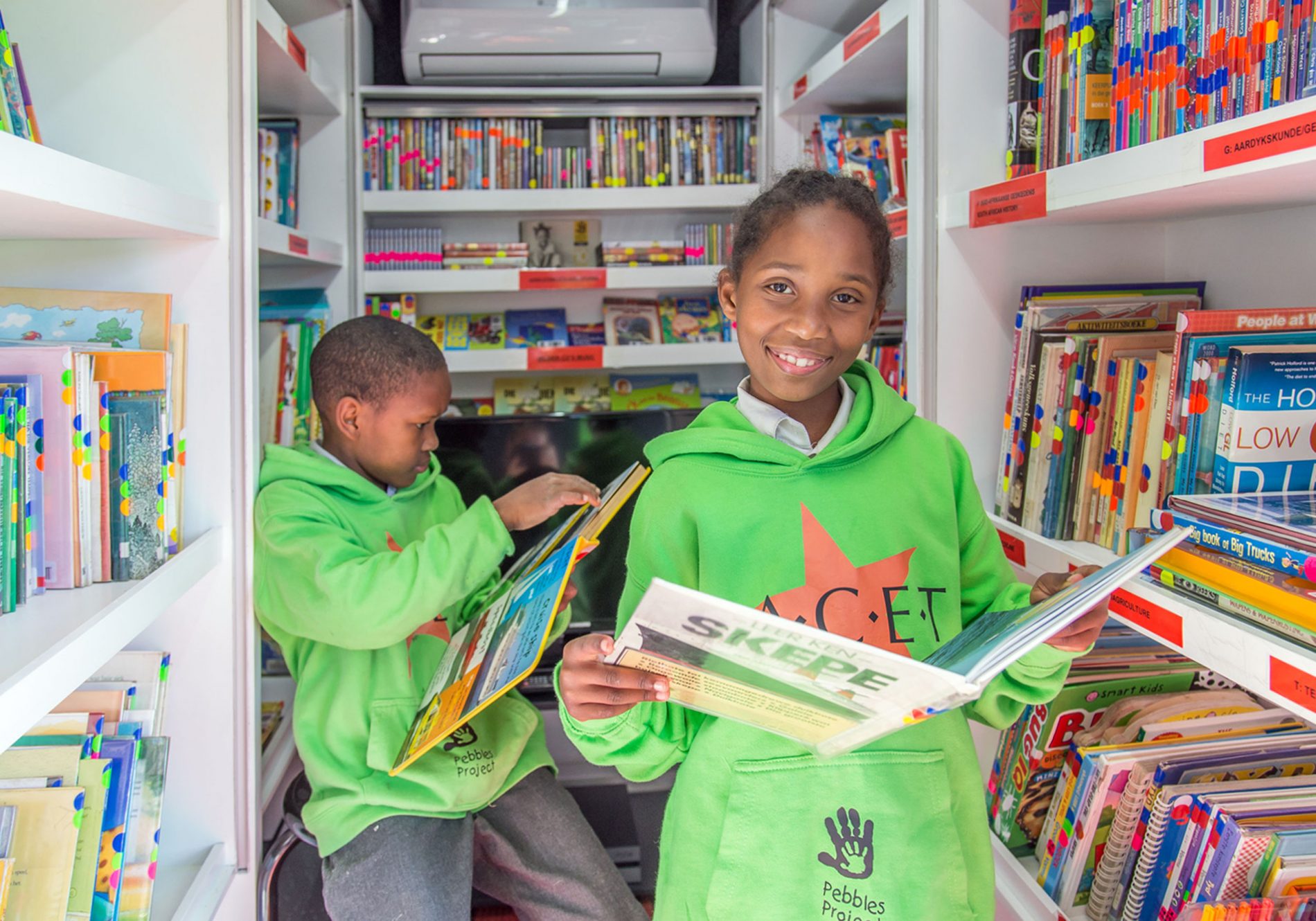 Two children reading books in a FACET mobile reading library