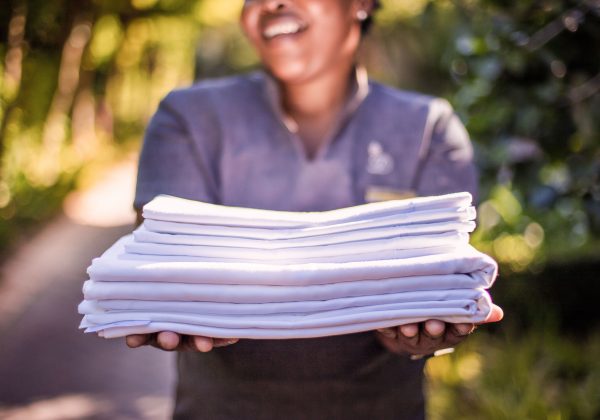 A lady from room service smiling holding a stack of fresh linens