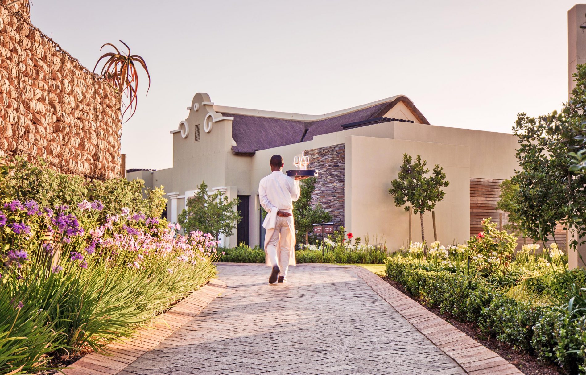 A waiter carrying a wine bottle on a tray to a Delaire Graff Lodge