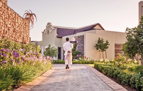 A waiter carrying a wine bottle on a tray to a Delaire Graff Lodge